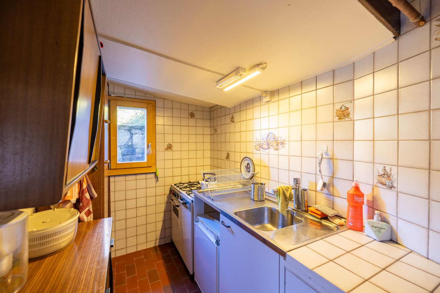 Cuisine équipée du mayen : plan de travail carrelé, évier inox, cuisinière à gaz, fenêtre sur la montagne.
