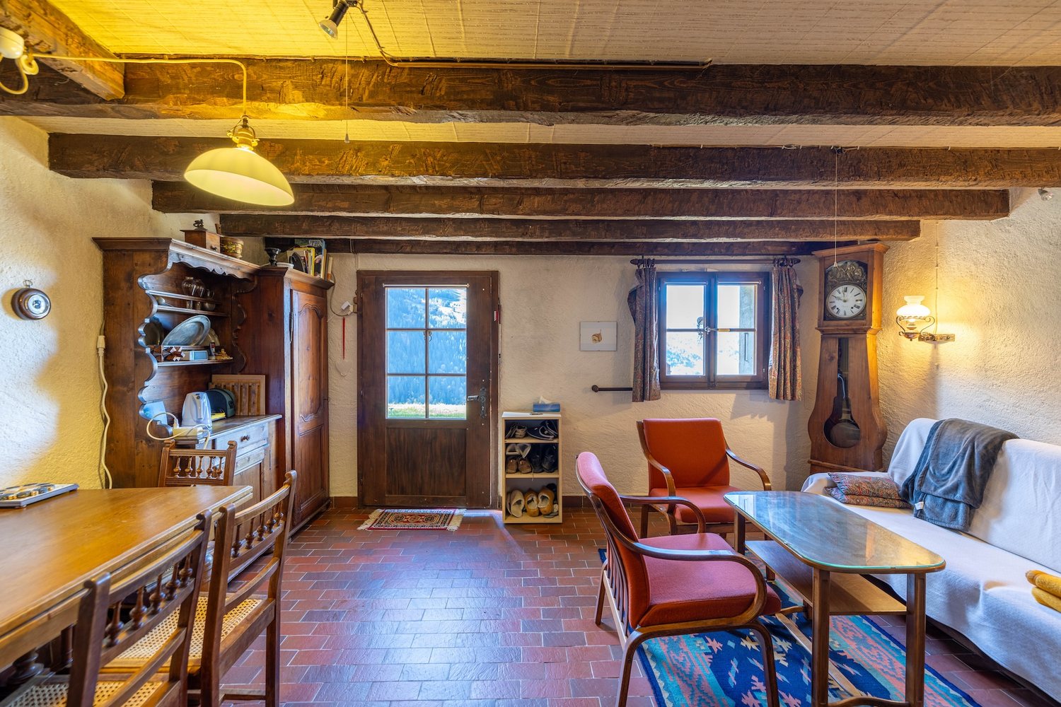 Coin à manger du mayen : grande table en bois et chaises, vaisselier, porte vitrée ouvrant sur la terrasse et la vallée.