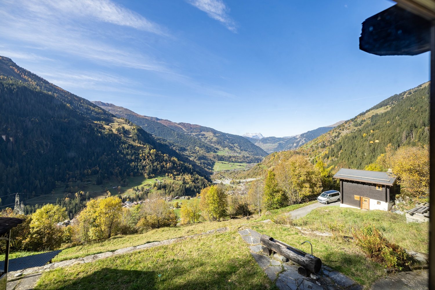 Vue depuis le pré du mayen : la vallée de Bagnes, les forêts et les sommets enneigés au loin, le couvert à voiture à droite.
